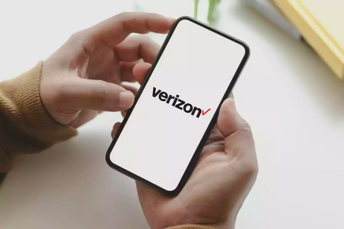 Person holding a mobile phone displaying the Verizon logo on the screen. Person holding a mobile phone displaying the Verizon logo on the screen.