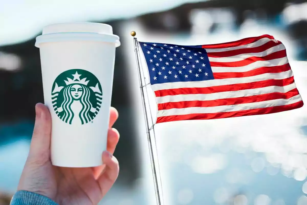 A hand holds a Starbucks coffee cup next to a waving American flag.