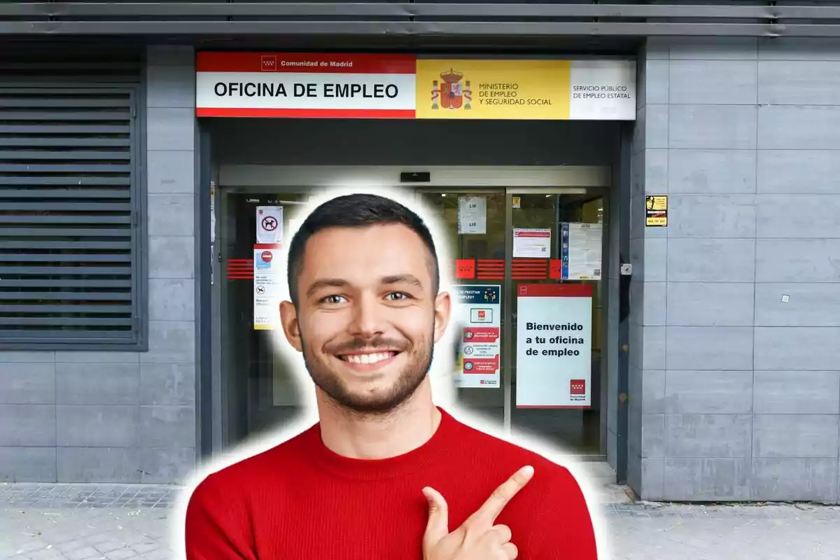 Un home somrient amb un suèter vermell assenyala amb el dit cap a l?entrada d?una oficina d?ocupació a Madrid.