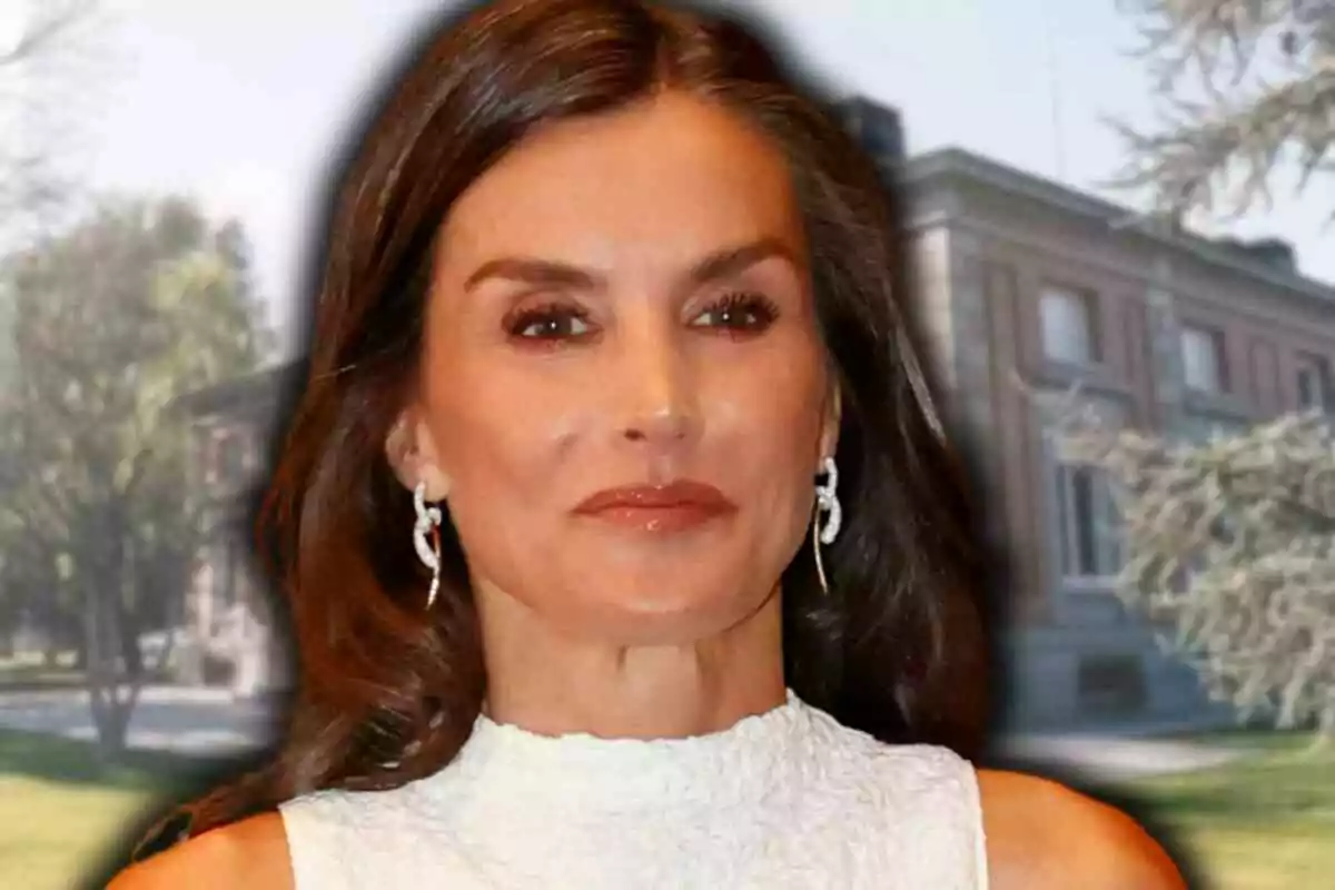 La reina Letizia de cabello castaño largo y suelto con vestido blanco sin mangas y pendientes plateados posando frente al edificio de la Zarzuela rodeado de árboles