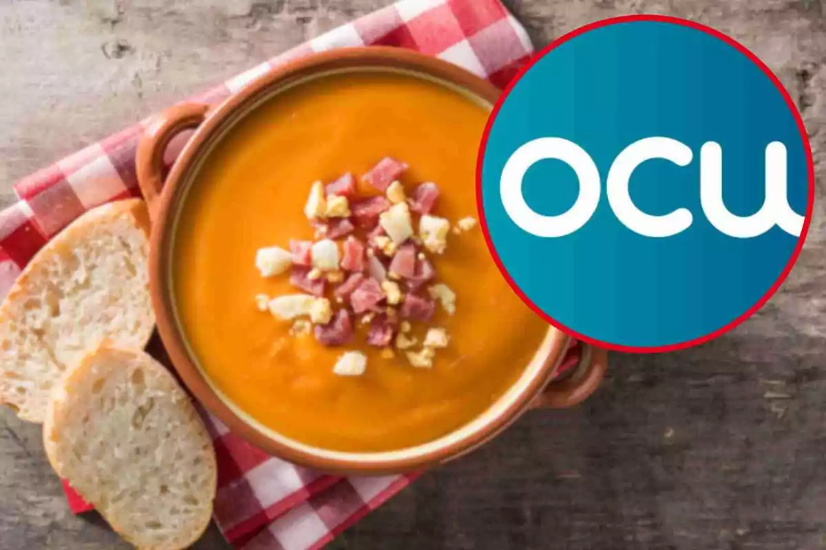 Un plat de sopa de color taronja amb trossos de pernil i ou al centre acompanyat de llesques de pa sobre un estovalles de quadres vermells i blancs amb un logotip circular blau i blanc a la cantonada. Un plat de sopa de color taronja amb trossos de pernil i ou al centre acompanyat de llesques de pa sobre un estovalles de quadres vermells i blancs amb un logotip circular blau i blanc a la cantonada.