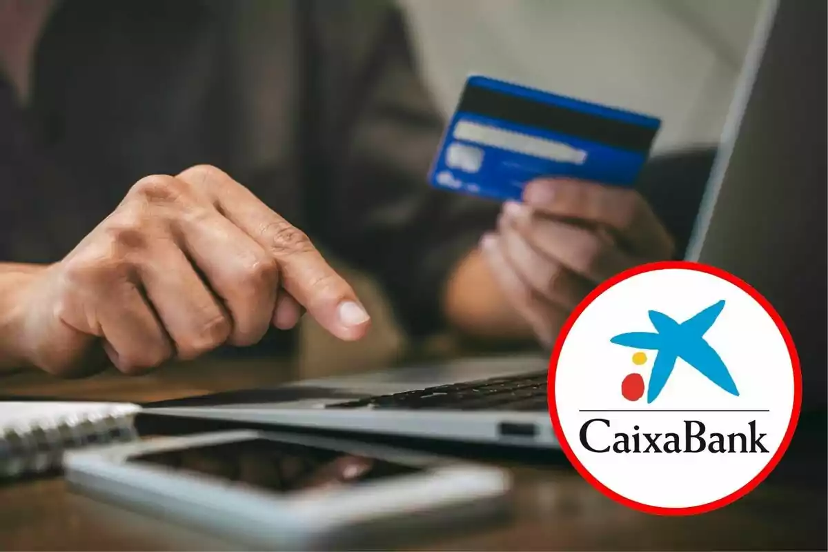 Persona usant una targeta de crèdit davant un ordinador portàtil amb el logotip de CaixaBank en primer pla.