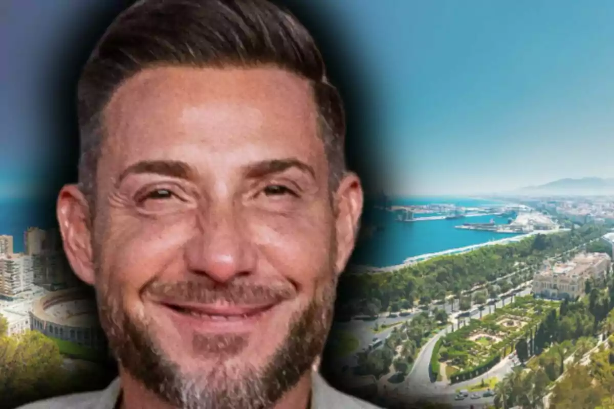 Imatge d'Antonio David Flores somrient amb barba i cabell curt que apareix en primer pla amb un fons d'una ciutat costanera i un port, que és Màlaga.