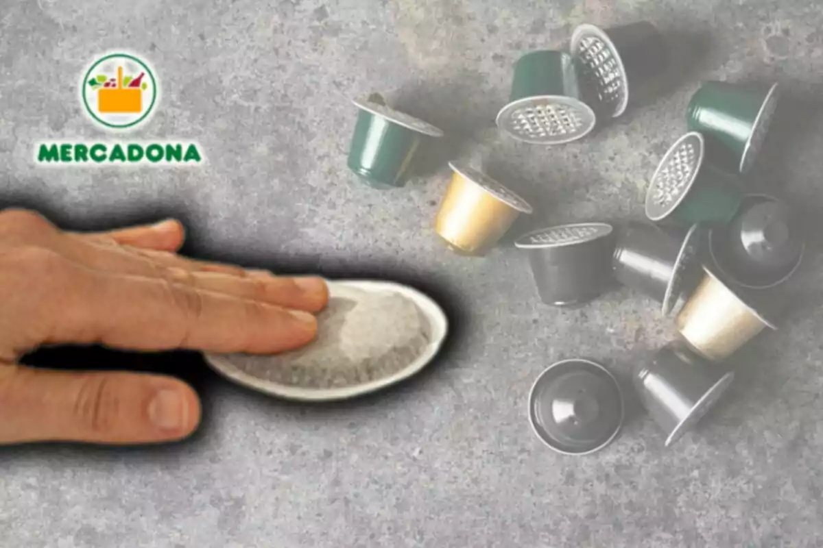 Una mà sosté una càpsula de cafè mentre altres càpsules estan escampades sobre una superfície grisa, amb un logotip a la cantonada superior esquerra. Una mà sosté una càpsula de cafè mentre altres càpsules estan escampades sobre una superfície grisa, amb un logotip a la cantonada superior esquerra.