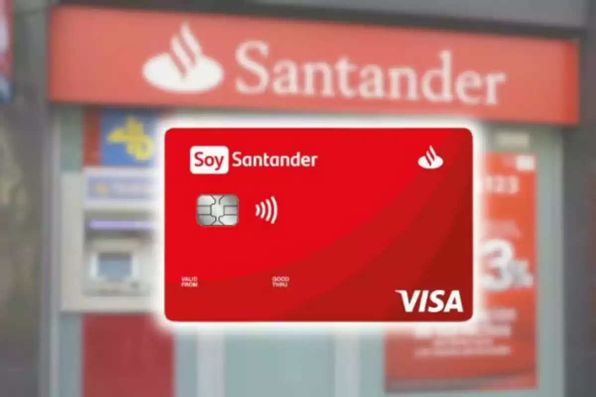 Targeta de crèdit vermella amb el logotip de Santander i Visa davant d'una sucursal del banc.