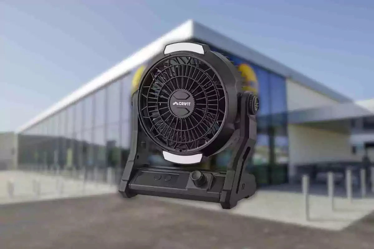 Un ventilador portátil negro de la marca Crivit frente a un edificio moderno con fachada de vidrio.