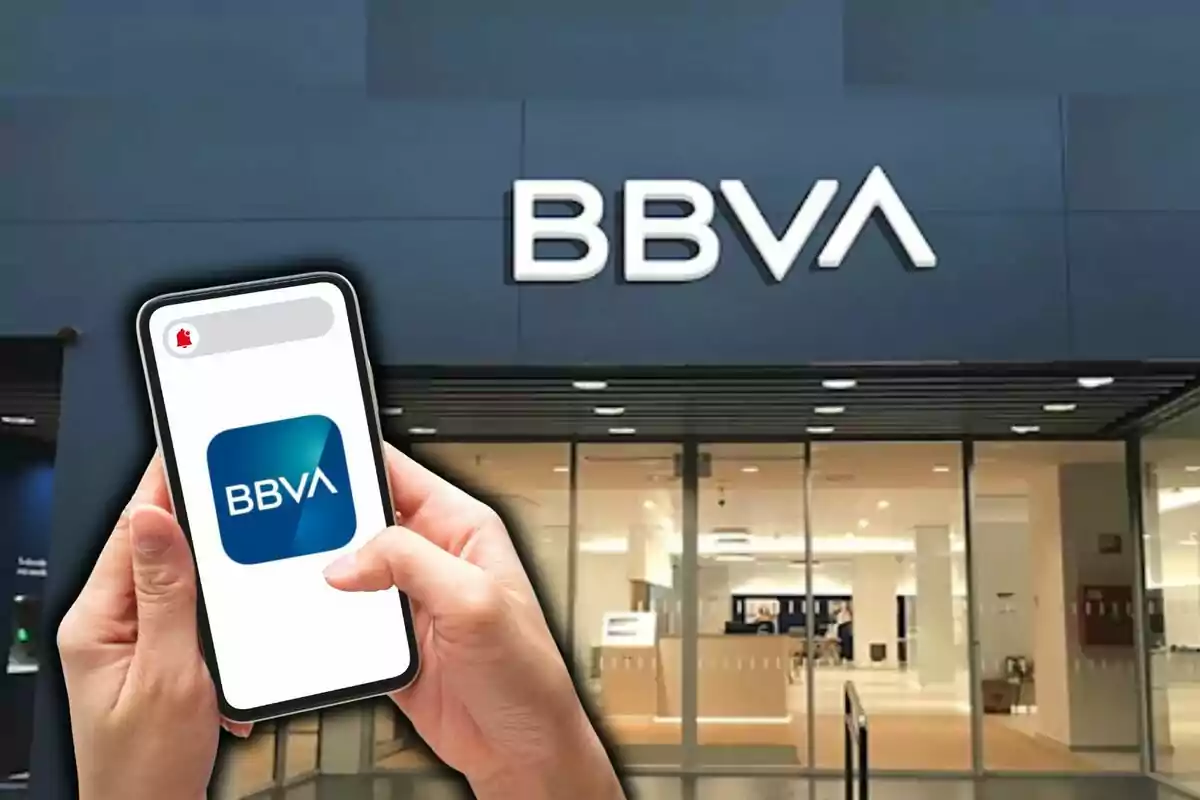 Una persona sosté un telèfon mòbil amb el logotip de BBVA davant d'una sucursal del banc.