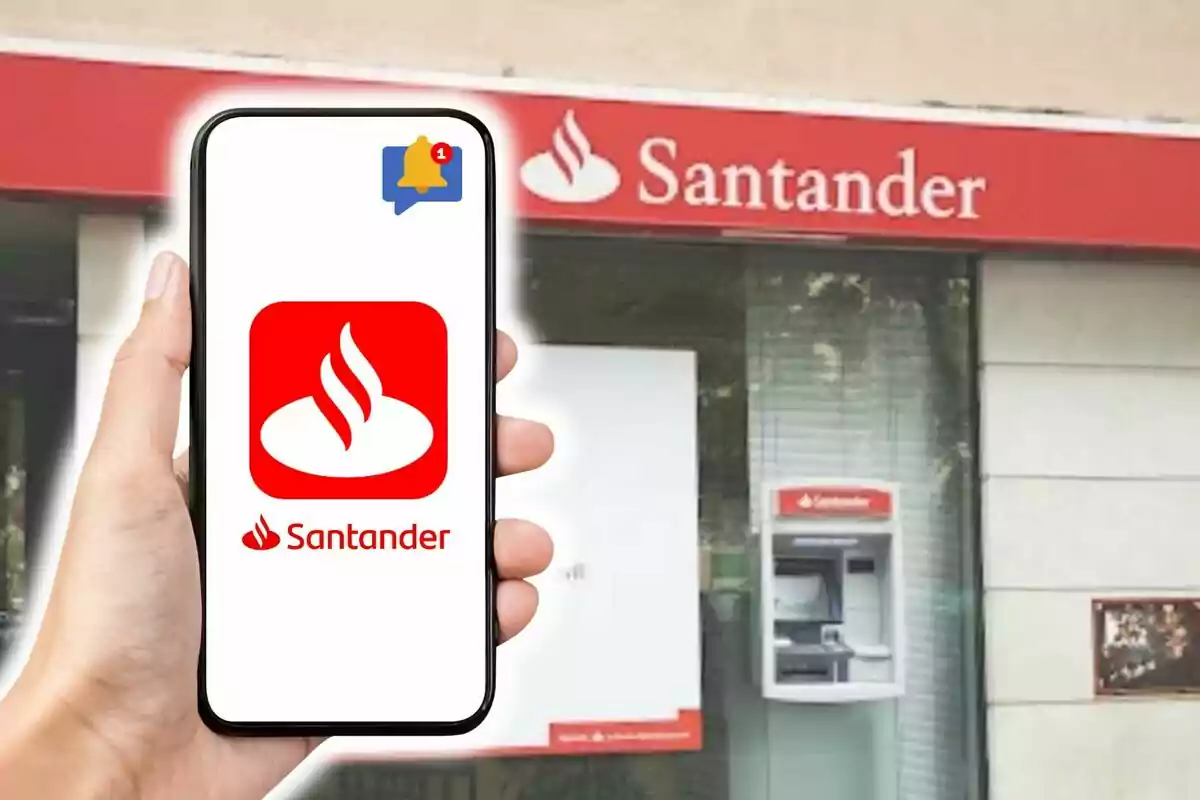 Una mà sosté un telèfon mòbil que mostra el logotip de Santander amb una notificació mentre al fons es veu una sucursal del banc amb un caixer automàtic.