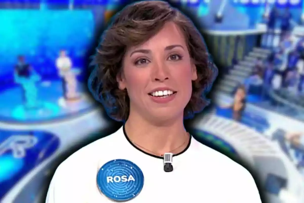 Rosa, concursant de 'Pasapalabra', somrient amb cabells curts i arrissats porta una samarreta blanca amb un micròfon i una etiqueta que diu "Rosa" en un entorn de programa de televisió amb un fons blau desenfocat.