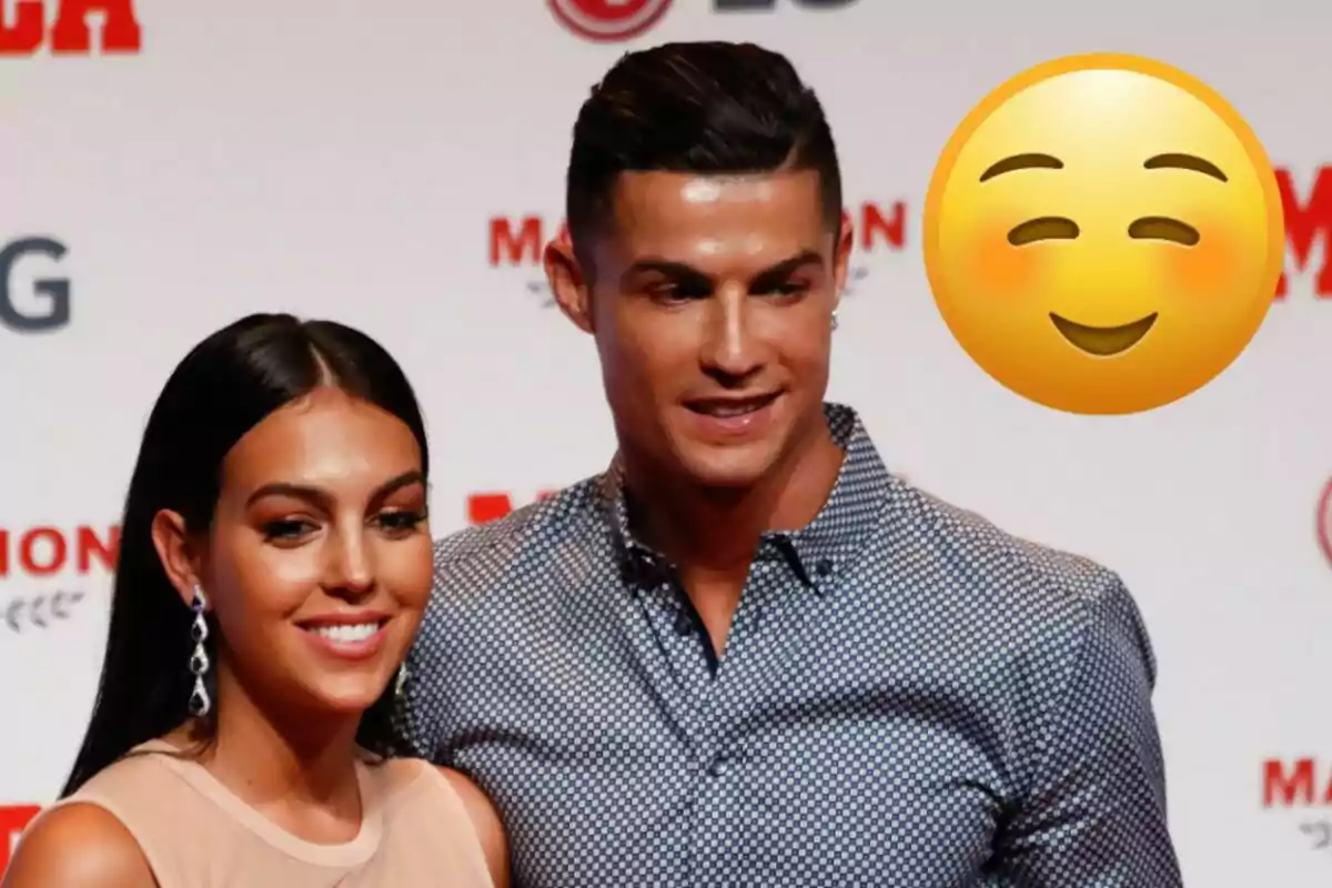 Georgina Rodríguez i Cristiano Ronaldo posant somrients en un esdeveniment amb un emoji de cara somrient al fons