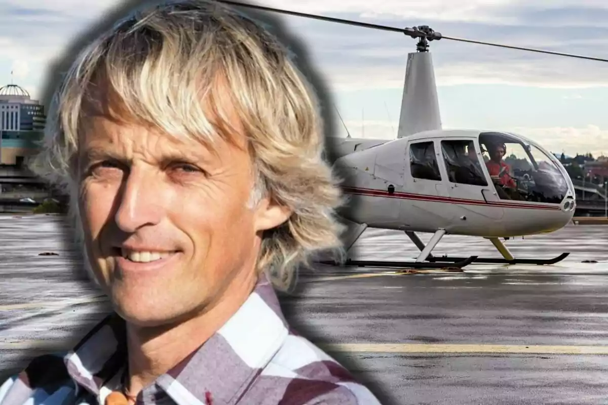 Jesús Calleja amb camisa de quadres en primer pla i un helicòpter blanc estacionat en un heliport al fons