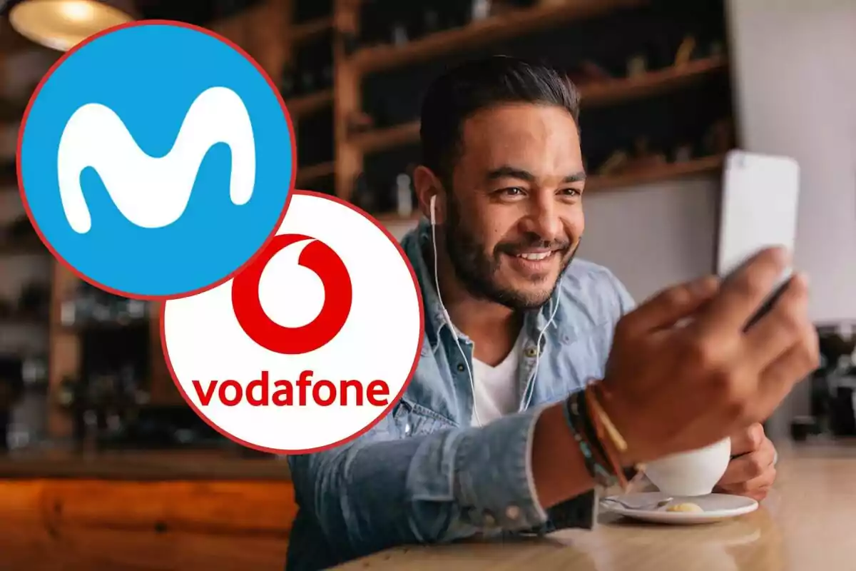 Un home somrient amb auriculars sosté un telèfon mòbil mentre està assegut en una cafeteria, amb els logotips de Movistar i Vodafone superposats a la imatge.