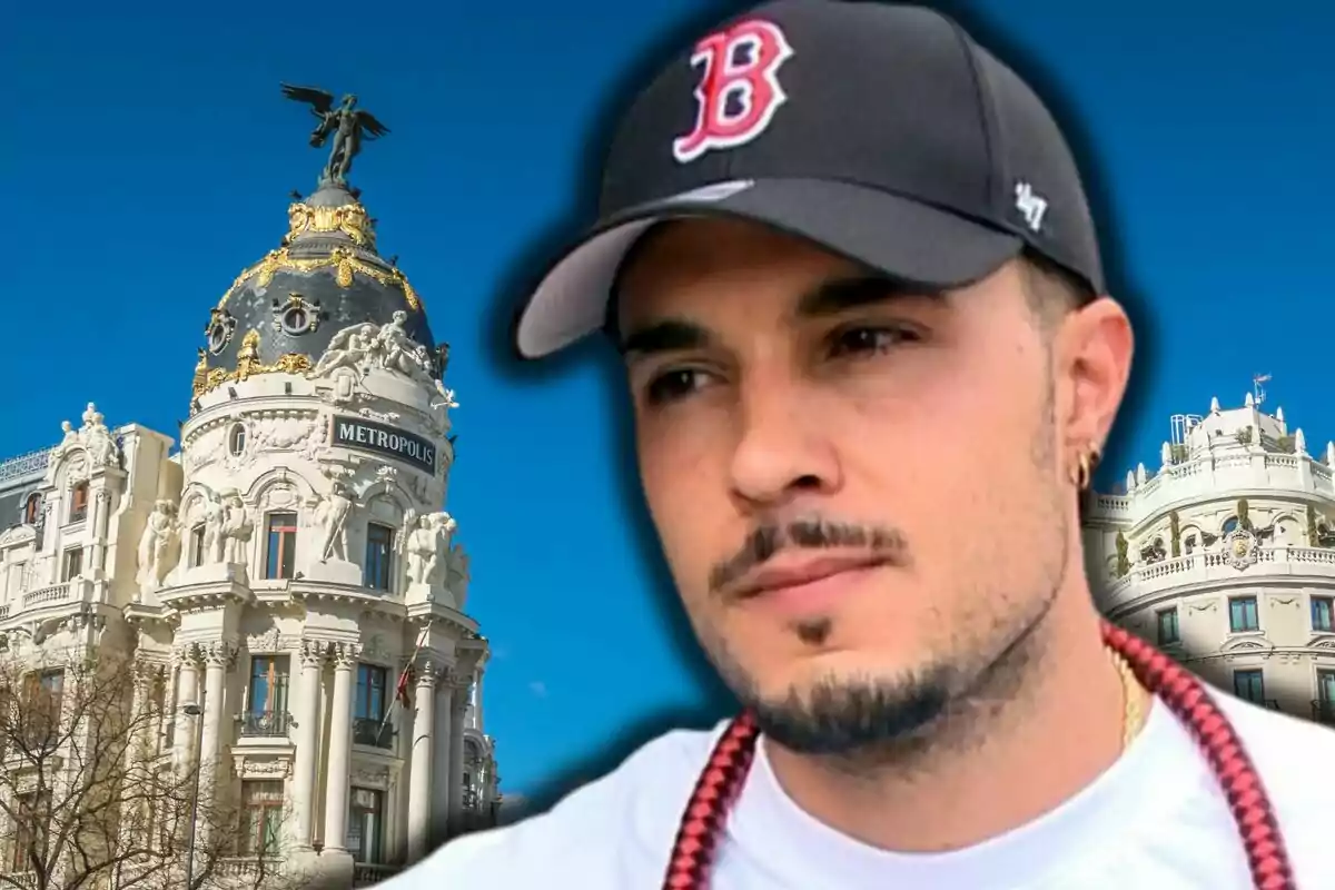 Carlo Costanzia con gorra negra y barba recortada en primer plano con el edificio Metrópolis de Madrid al fondo bajo un cielo azul