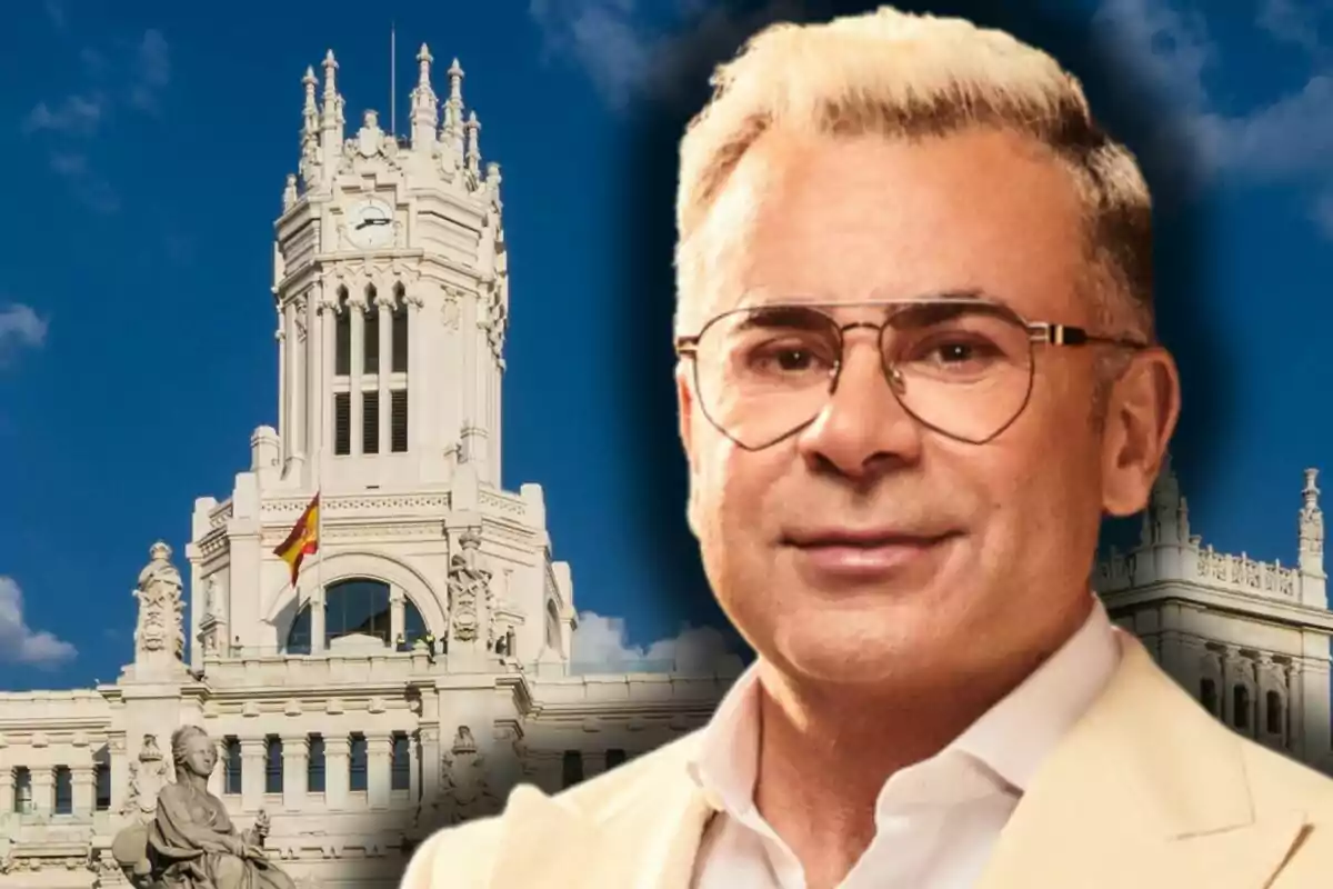 Jorge Javier Vázquez amb jaqueta clara davant d’un edifici històric blanc amb una bandera d’Espanya i cel blau de fons