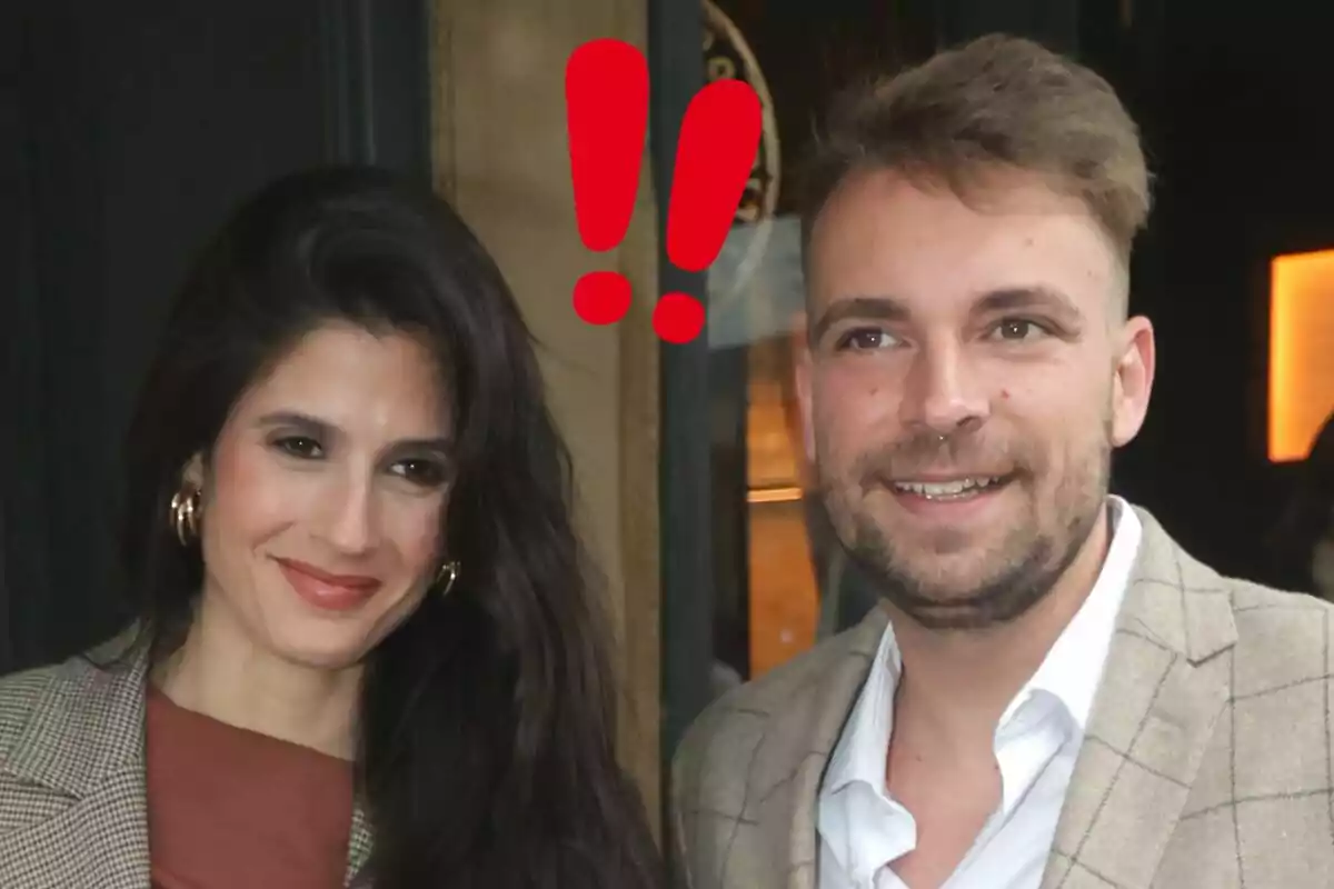 María Sánchez i José María Almoguera somriuen junts mentre posen per a una foto, tots dos vestits de manera elegant i amb dos signes d’exclamació vermells sobre els seus caps.