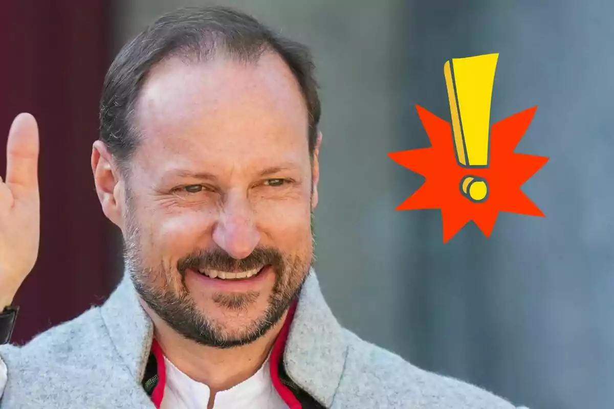 Haakon of Norway smiling with a beard and short hair raising his hand next to a yellow exclamation mark on a gray background.