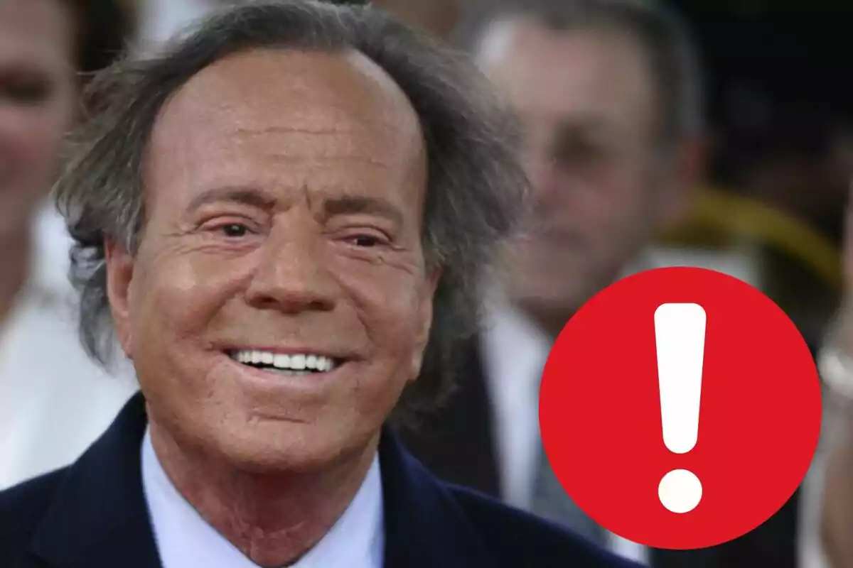 Julio Iglesias somrient amb una icona d'exclamació vermella a la cantonada inferior dreta.