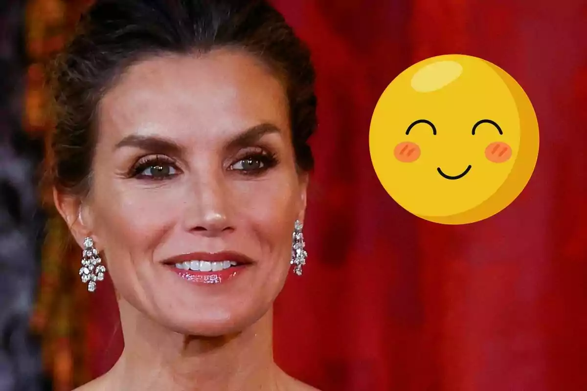 La reina Letícia amb arracades brillants somriu davant d'un fons vermell, acompanyada d'un emoji somrient.