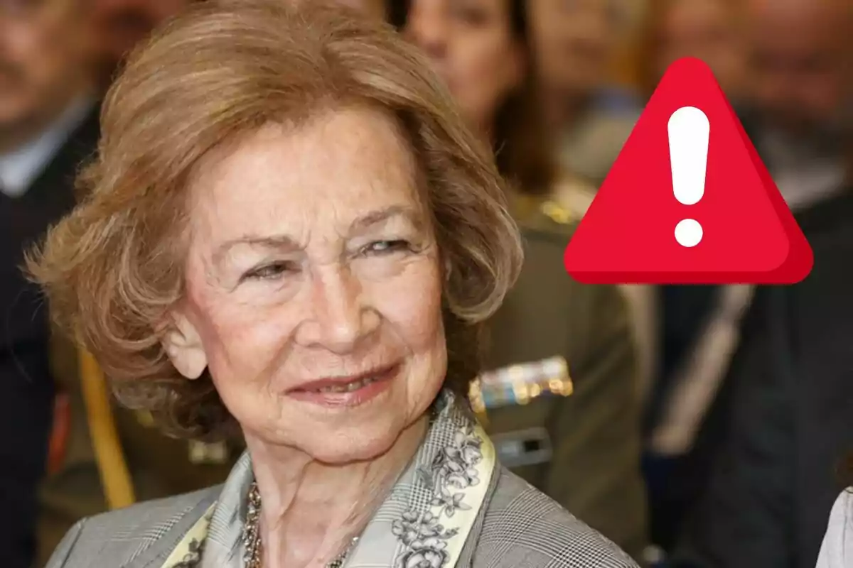 La reina Sofia somrient amb una icona d'advertència vermella al costat.