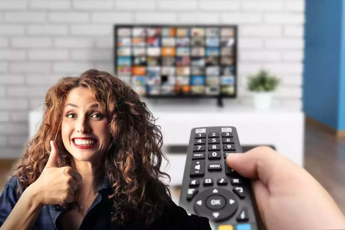 A person holds a remote control and a TV in the background, while on the left a woman gives a thumbs up, smiling
