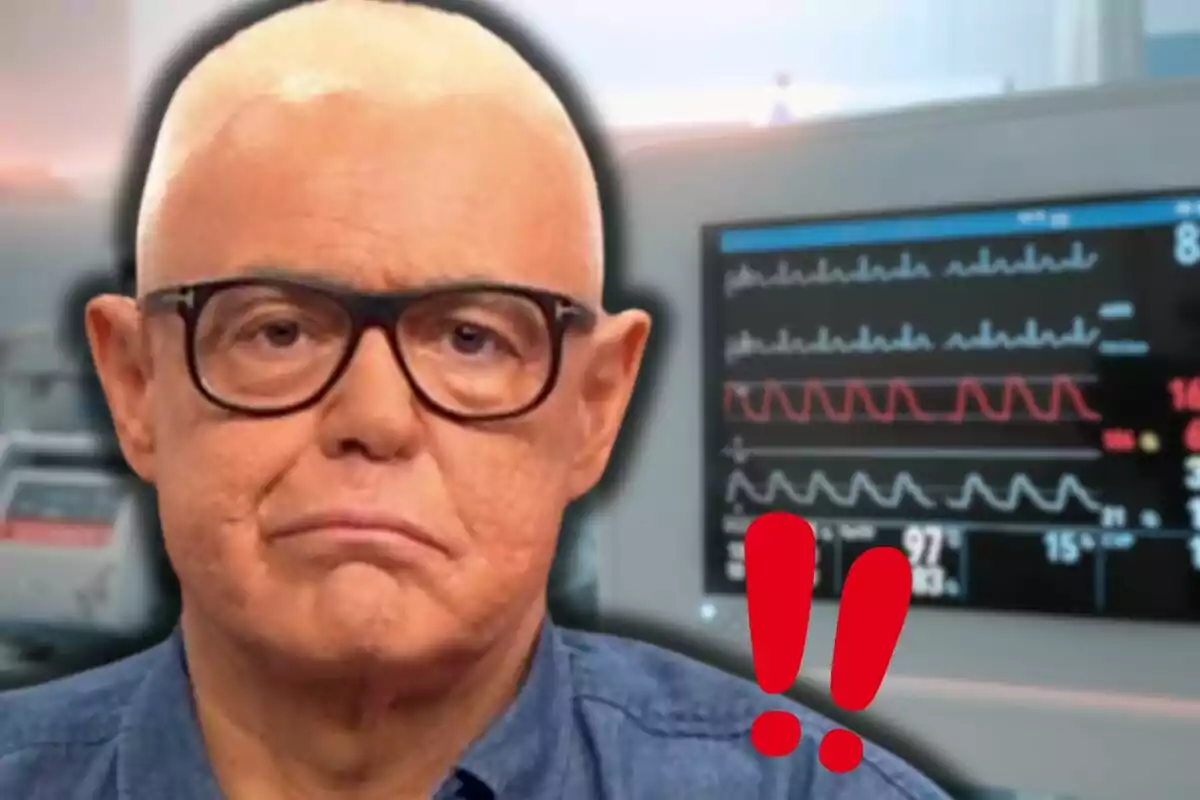 Un home amb ulleres i expressió seriosa davant d'un monitor de signes vitals amb signes d'exclamació vermells.