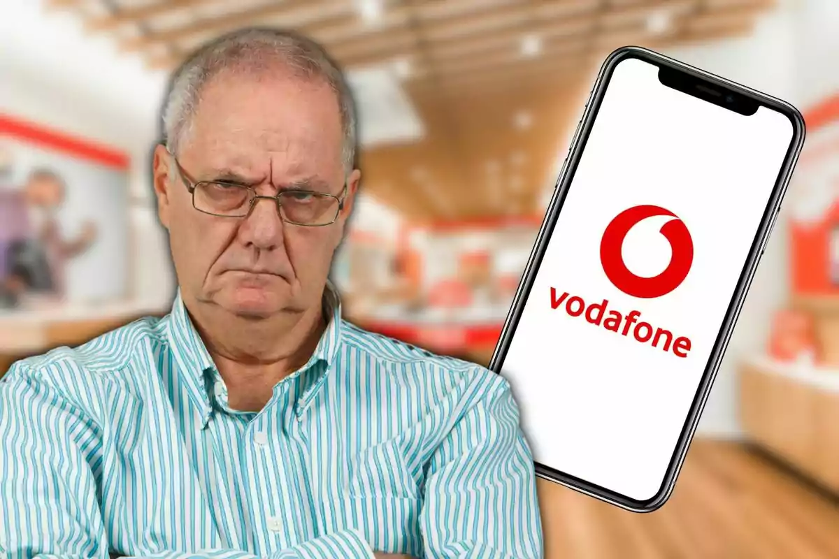 Un home gran amb expressió seriosa i braços plegats, amb un telèfon mòbil que mostra el logotip de Vodafone al fons d'una botiga.