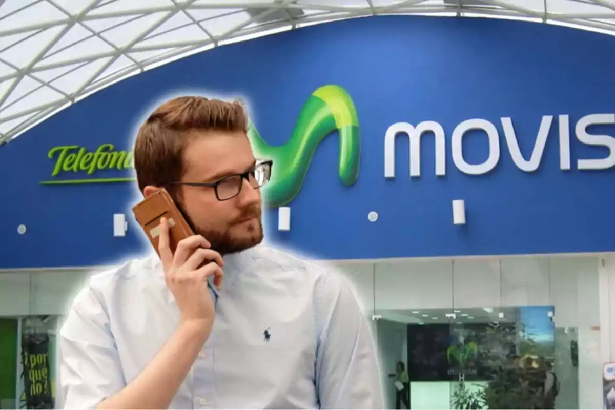 Un home amb ulleres i barba parla per telèfon davant d'una botiga de Movistar.
