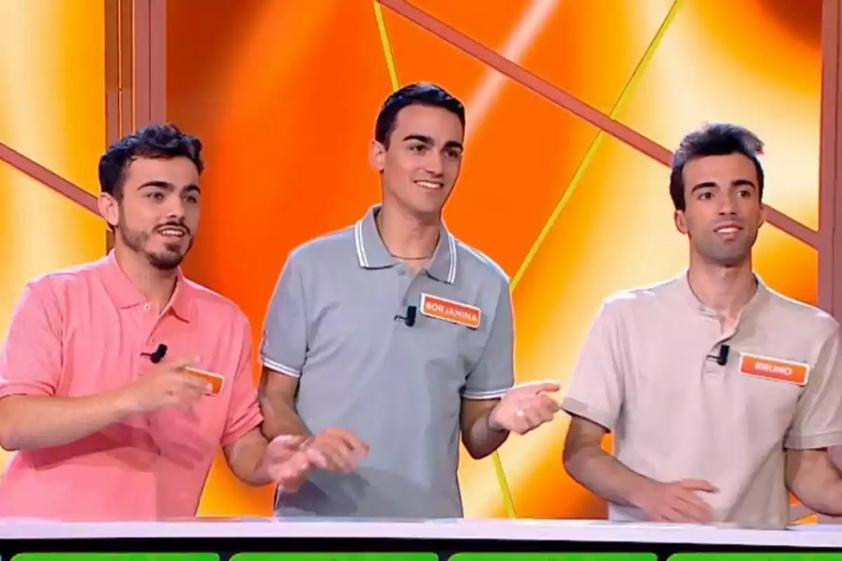 Els Mossos d'Arousa drets en un set de televisió amb fons taronja, cadascun amb una samarreta de diferent color i una etiqueta amb el seu nom. Els Mossos d'Arousa drets en un set de televisió amb fons taronja, cadascun amb una samarreta de diferent color i una etiqueta amb el seu nom.