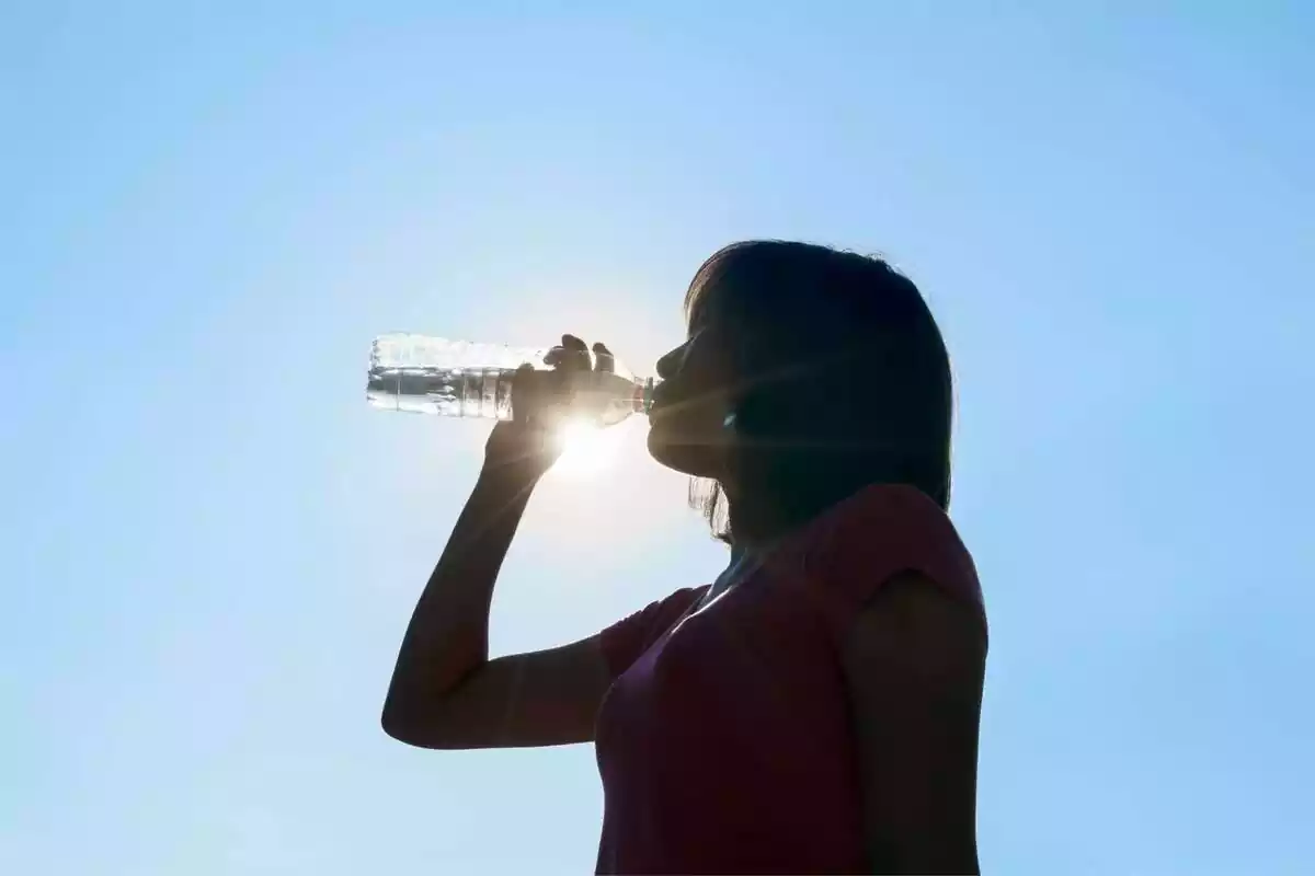 Dona amb samarreta rosa bevent aigua sota el sol