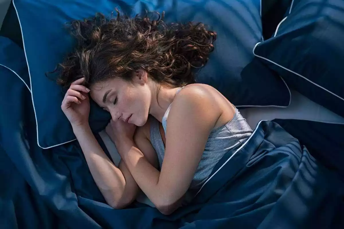 Dona dormint en un llit amb llençols de color blau marí