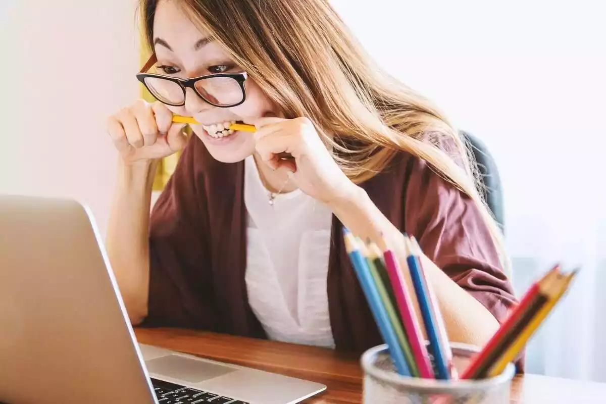 Una dona davant d'un ordinador portàtil molt nerviosa i amb un llapis a la boca