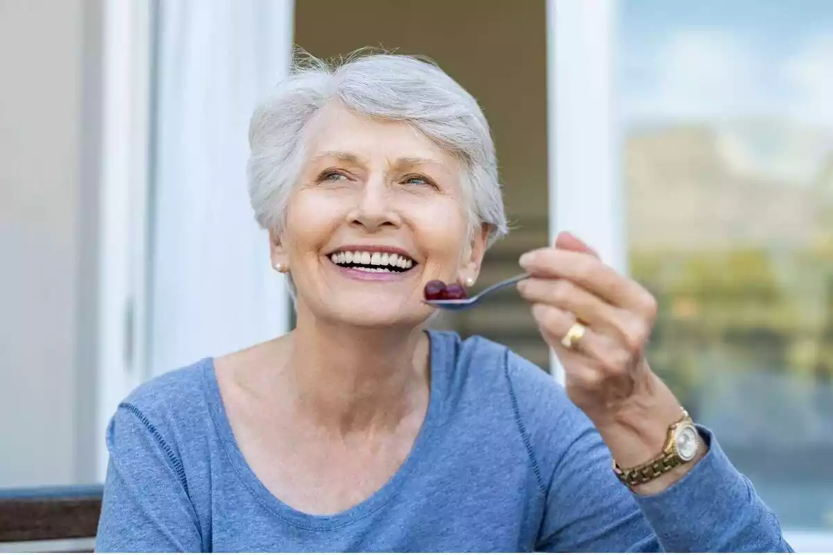 Dona gran somrient amb una cullera amb fruita a la mà