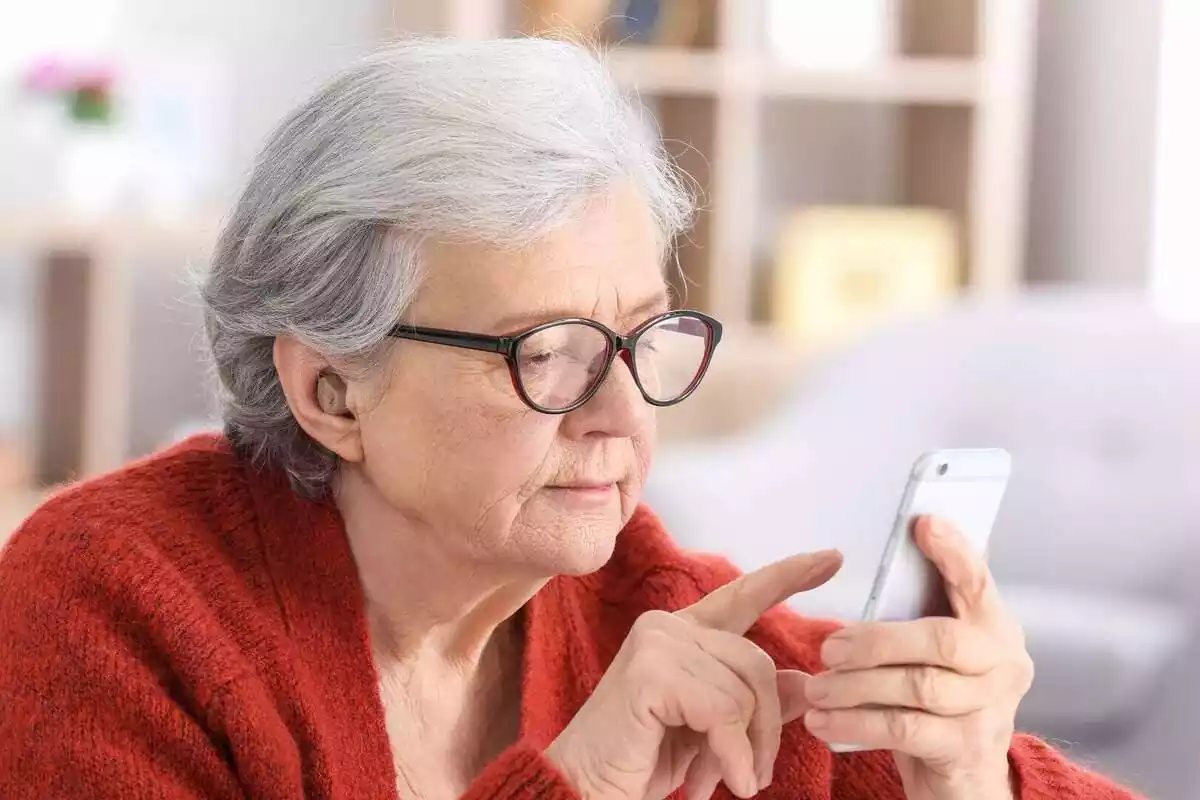 Una dona gran escrivint al seu telèfon mòbil amb les ulleres posades