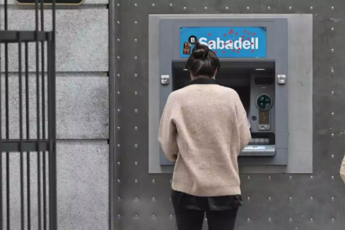 Persona d'esquena usant un caixer automàtic del banc Sabadell.