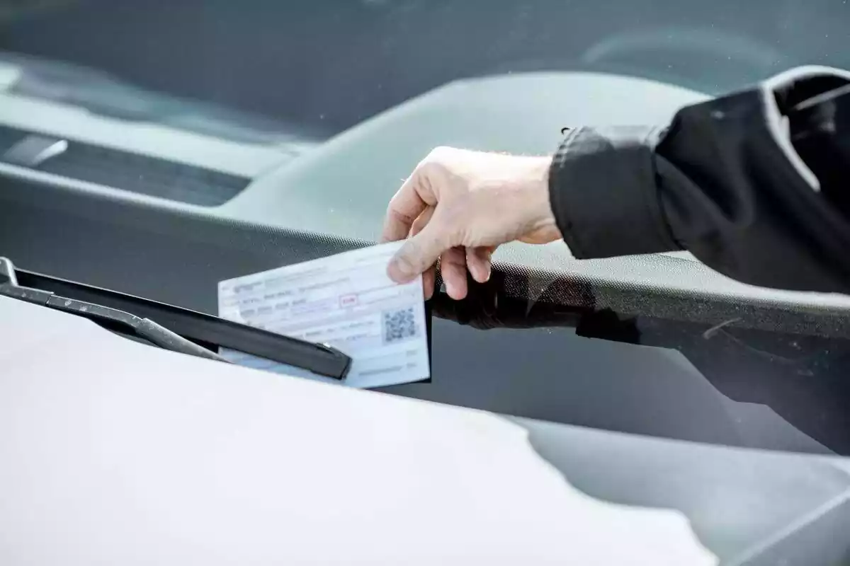 Una persona posant una multa a un cotxe