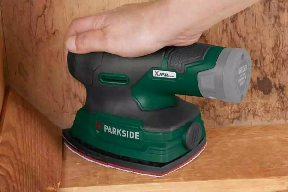 Una mà sostenint una polidora elèctrica verda i negra sobre una superfície de fusta. Una mà sostenint una polidora elèctrica verda i negra sobre una superfície de fusta.