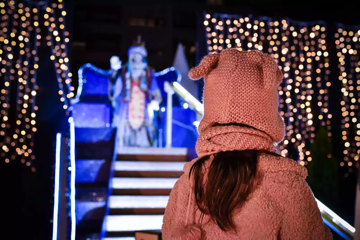 Una persona amb gorra de llana observa una figura il·luminada en un entorn festiu nocturn.