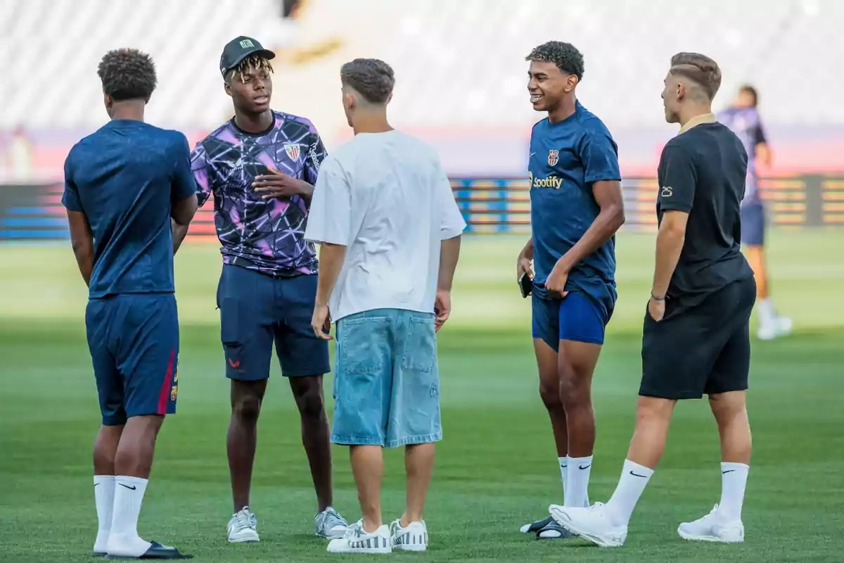 Un grupo de cinco jóvenes está de pie en un campo de fútbol, conversando y riendo. Un grupo de cinco jóvenes está de pie en un campo de fútbol, conversando y riendo.