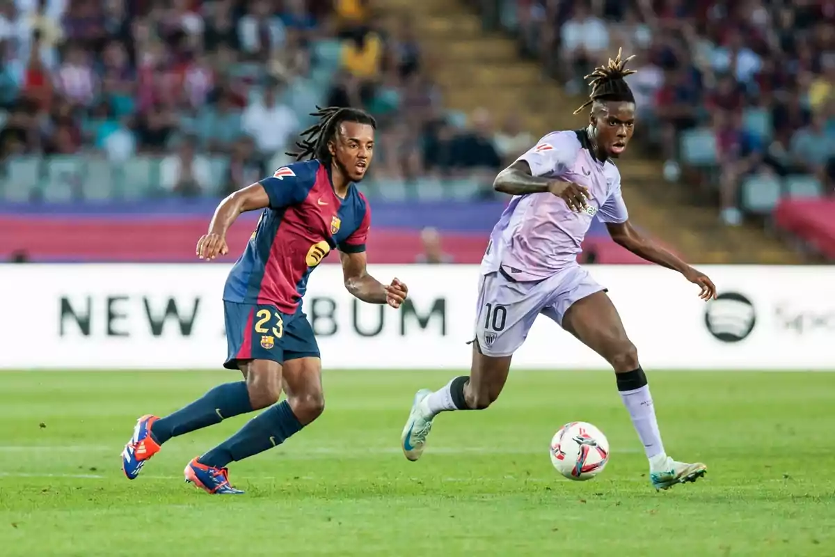 Dos jugadores de fútbol compiten por el balón en un partido, uno con el uniforme del FC Barcelona y el otro con el uniforme del equipo contrario. Dos jugadores de fútbol compiten por el balón en un partido, uno con el uniforme del FC Barcelona y el otro con el uniforme del equipo contrario.