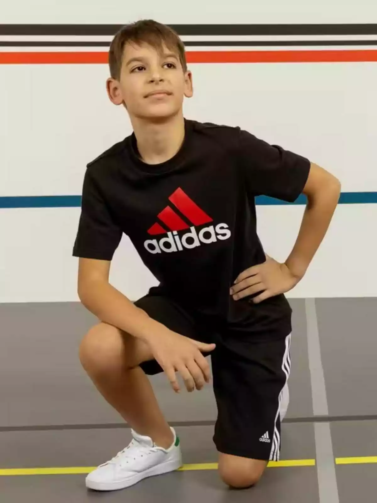 Un nen amb roba esportiva negra d?Adidas posa en una pista d?esports.