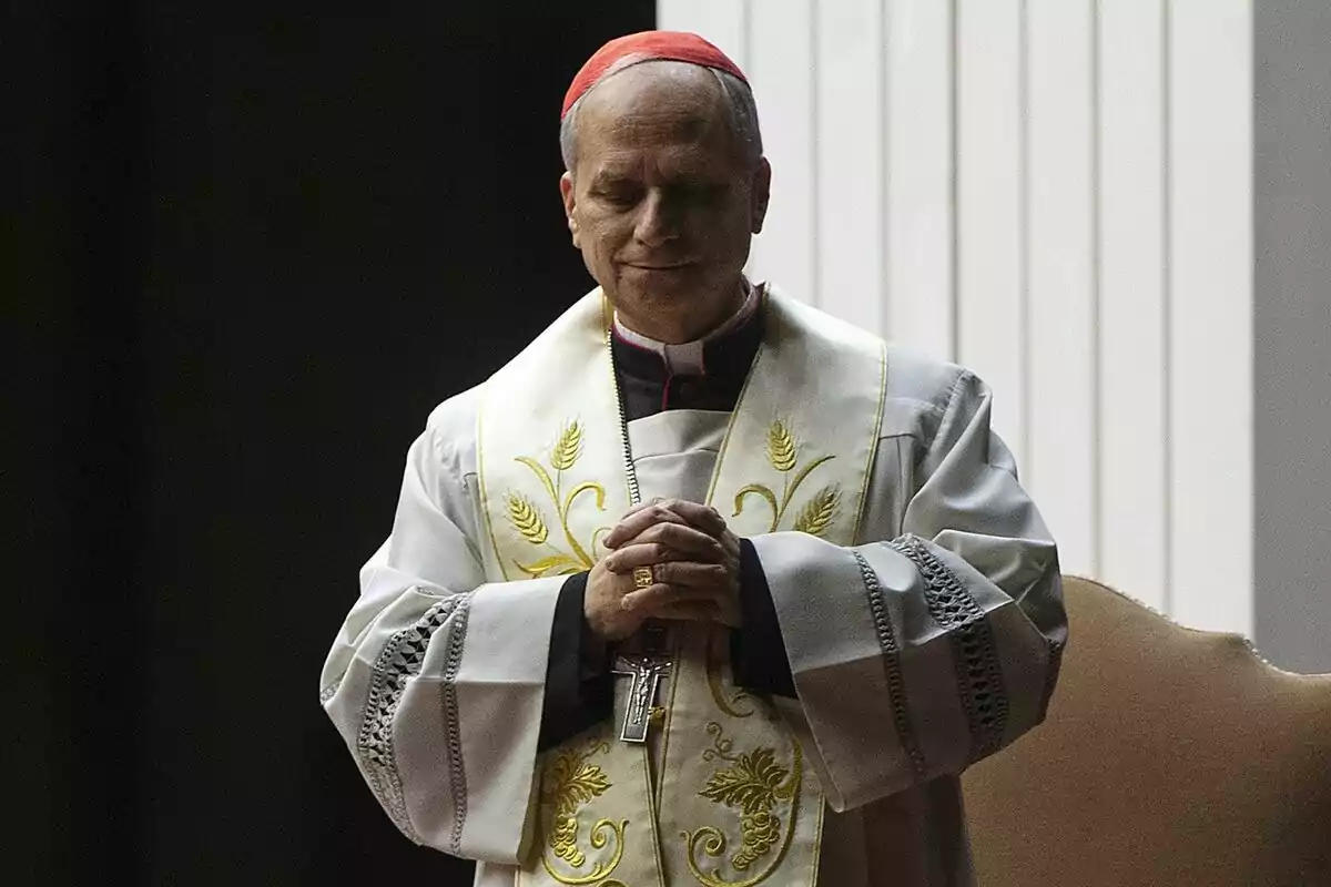 A cleric in white religious attire with golden details stands with hands together in a prayerful attitude. A cleric in white religious attire with golden details stands with hands together in a prayerful attitude.