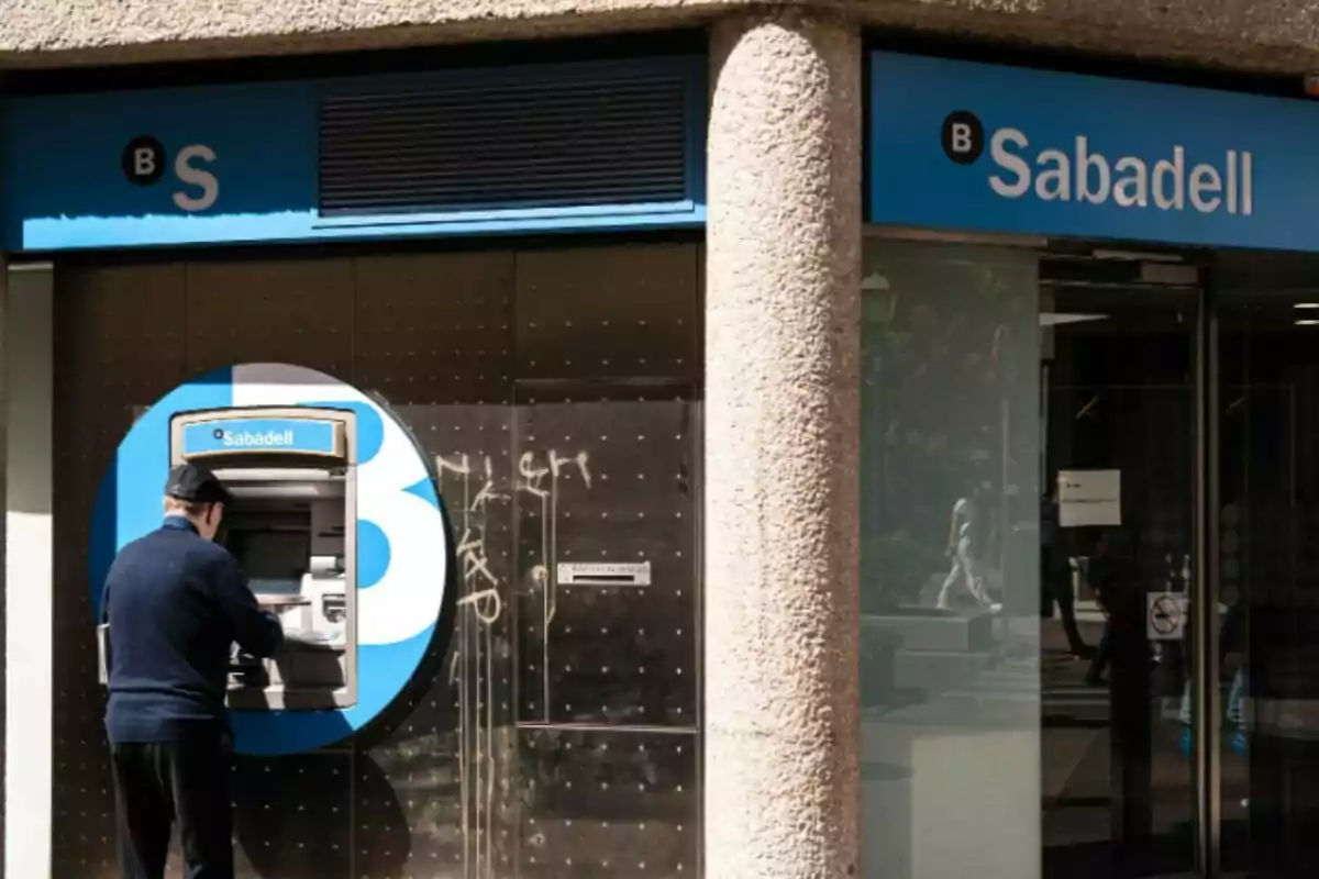 Un home usant un caixer automàtic d'un banc amb el logotip de Sabadell a la façana.