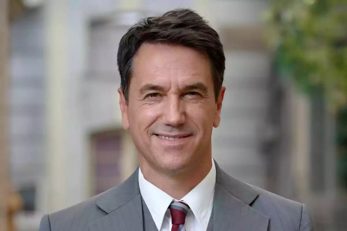 Oriol Tarrasón somrient amb vestit gris i corbata vermella en un entorn urbà a Amar es para siempre. Oriol Tarrasón somrient amb vestit gris i corbata vermella en un entorn urbà a Amar es para siempre.