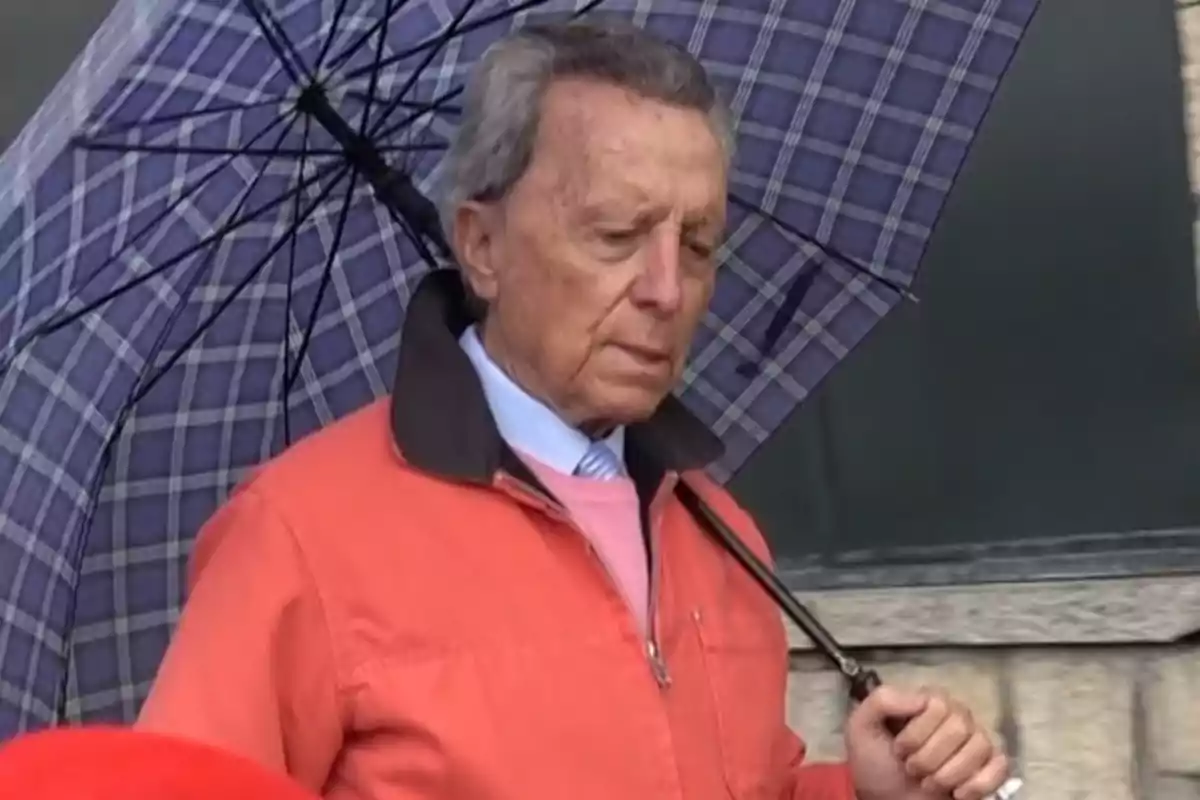 Ortega Cano amb jaqueta taronja sosté un paraigua de quadres. Ortega Cano amb jaqueta taronja sosté un paraigua de quadres.