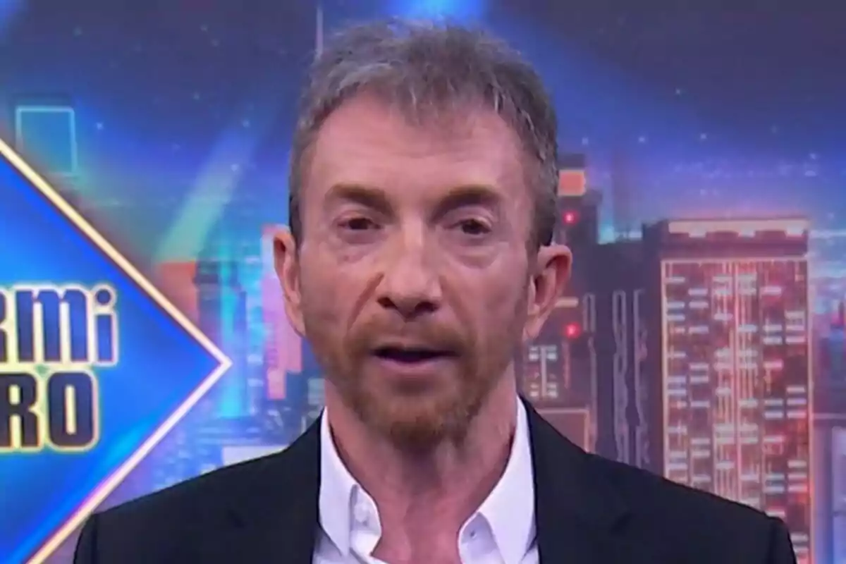 Pablo Motos con barba y cabello corto aparece en un programa de televisión con un fondo colorido y urbano en El Hormiguero. Pablo Motos con barba y cabello corto aparece en un programa de televisión con un fondo colorido y urbano en El Hormiguero.