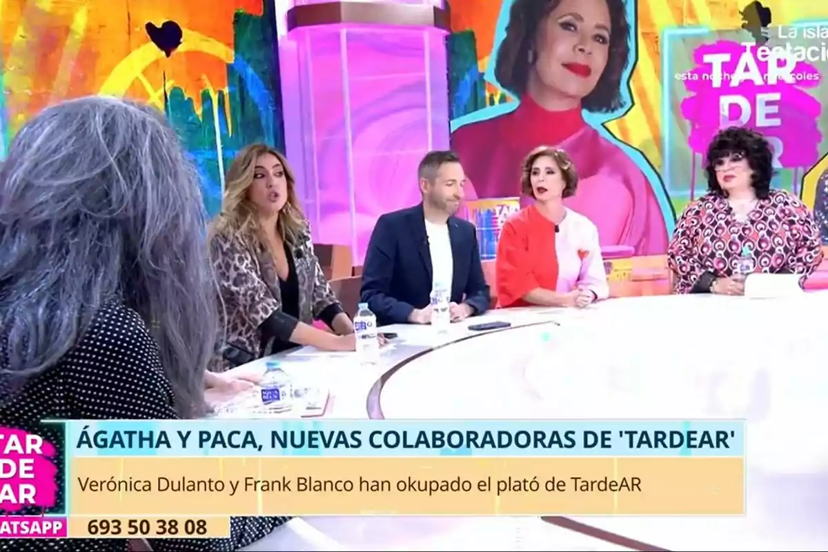 Mario Vaquerizo, Verónica Dulanto, Frank Blanco, Ágatha Ruiz de la Prada i Paca la Piraña estan asseguts al voltant d'una taula en un plató de TardeAR acolorit, amb un gran retrat d'una dona al fons.