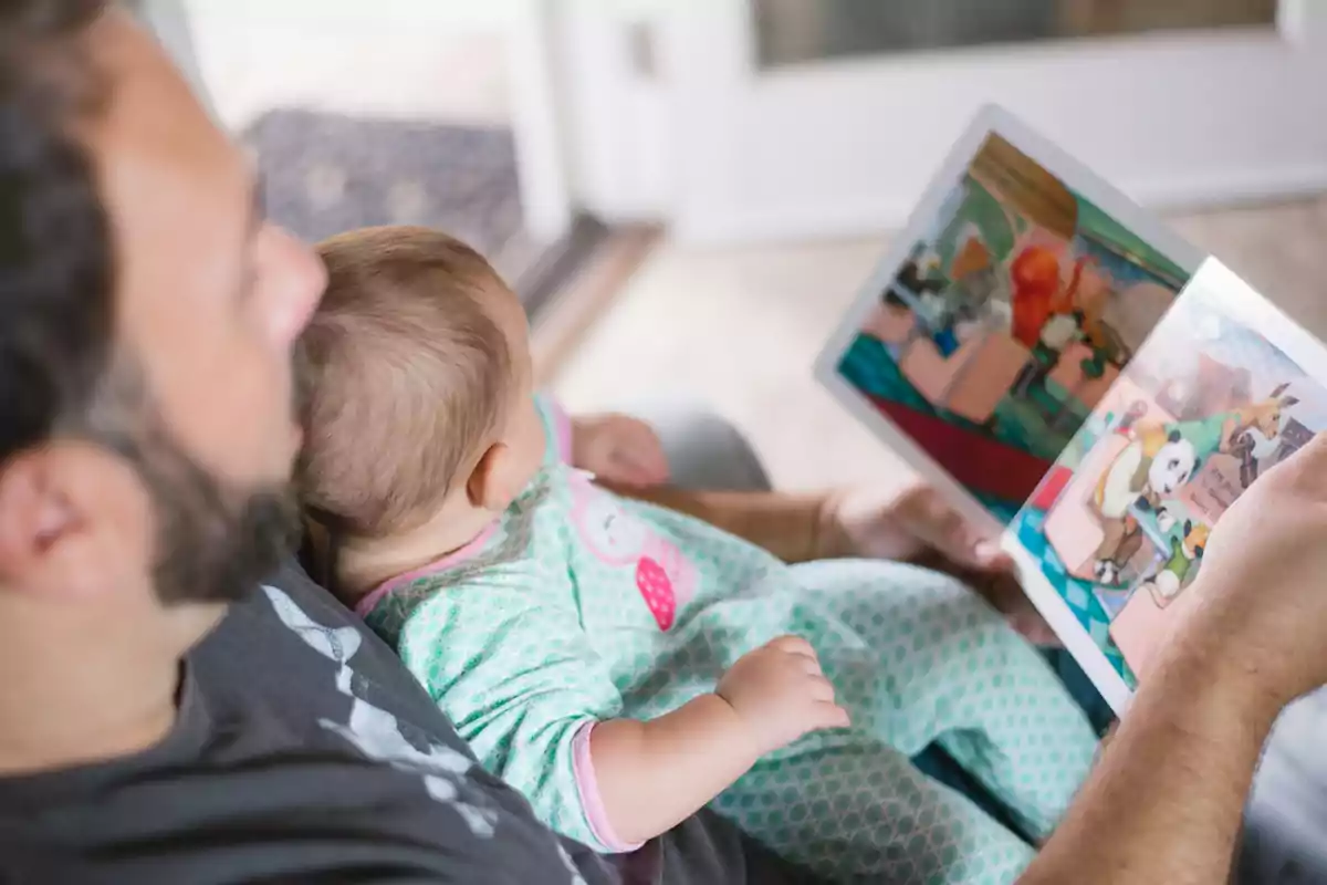Home llegint un llibre il·lustrat a un nadó assegut a la seva falda