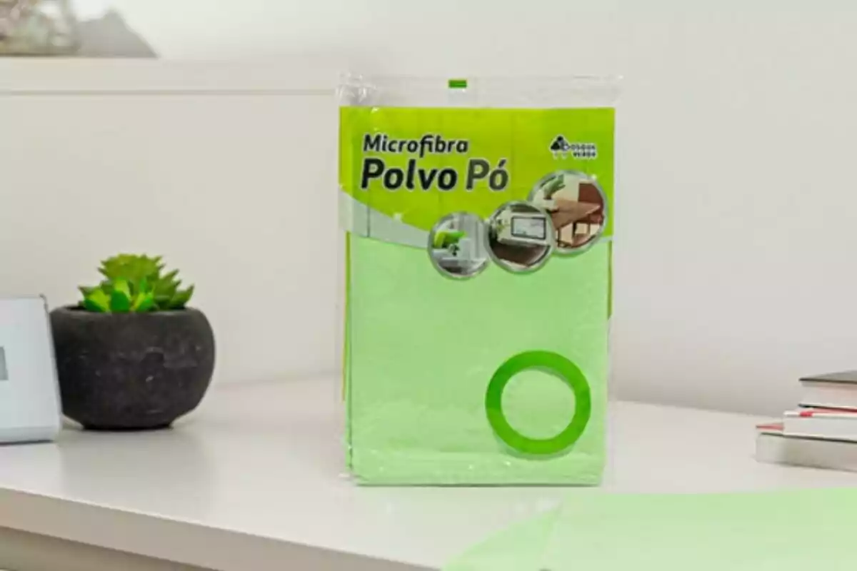 Paquete de paños de microfibra verde para limpieza sobre una mesa blanca junto a una planta en maceta negra.