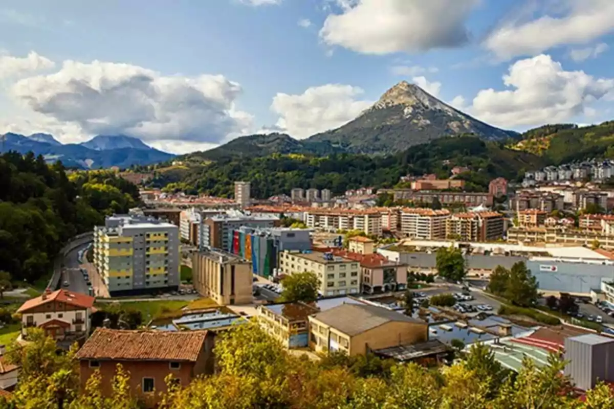 Vista panoràmica d'una ciutat envoltada de muntanyes amb edificis i un cel parcialment ennuvolat.