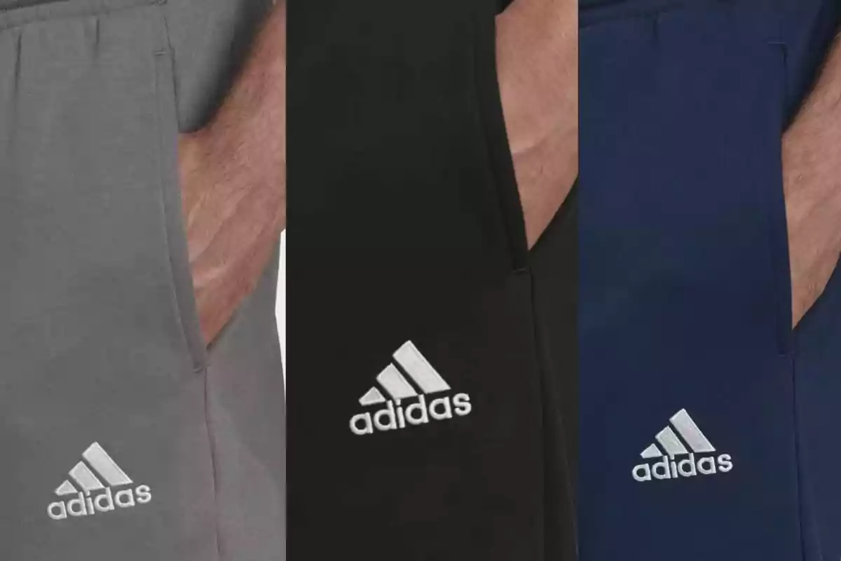 Tres pantalons esportius de la marca Adidas en colors gris, negre i blau, cadascun amb el logotip brodat en blanc.